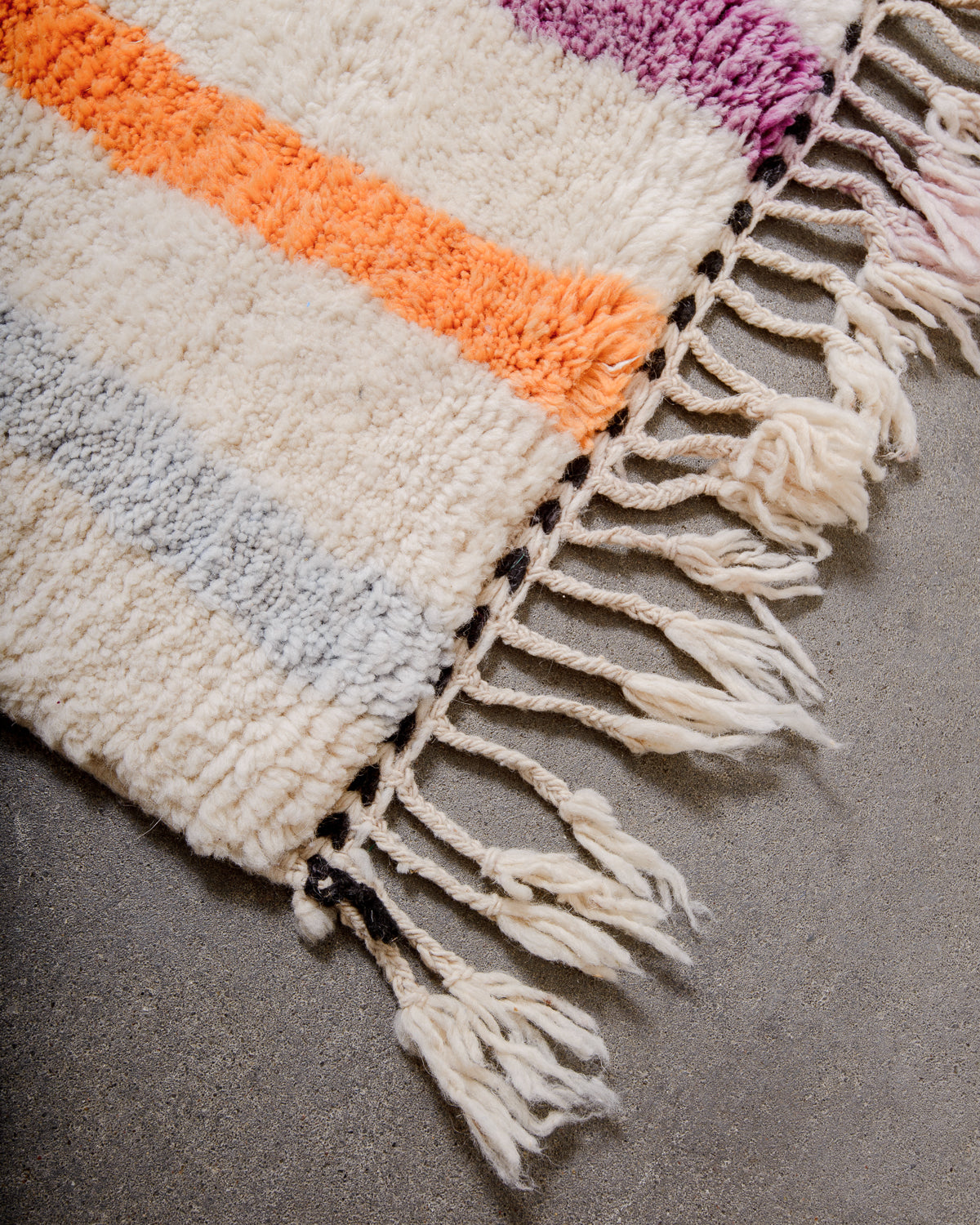 Corner of rug made of thick wool pile and natural wool tassels.